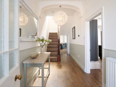 A hallway with wooden floor a table with flowers a carpeted staircase and a decorative ceiling light at Waves End in St Ives