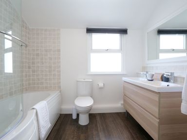 A bathroom with a bathtub shower combination toilet and double sink vanity with a mirror at Waves End in St Ives