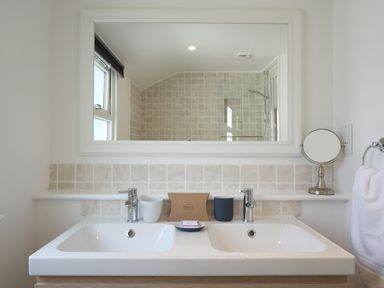 A bathroom sink with two faucets cups soap and a mirror above at Waves End in St Ives