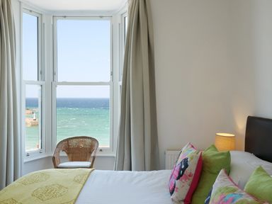 A bedroom with a bed with butterfly pillows and a window with a sea view at Waves End in St Ives