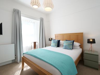 A bedroom with a wooden bed and teal bedding with pillows at Waves End in St Ives