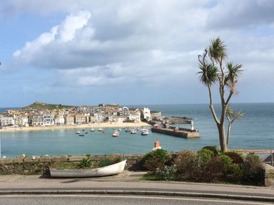 A coastal town with boats in the bay a stone wall and a tree in the foreground at Waves End in St Ives