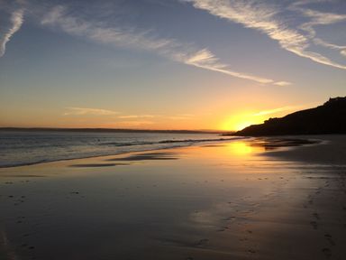 A beach with wet sand and footprints at sunset with the sun near the horizon and clouds in the sky at Waves End in St Ives