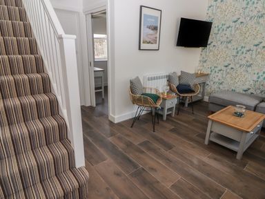 A sitting area with two wicker chairs cushions side tables mounted tv and stairs with striped carpet at Gwynfryn in Pen-Clawdd