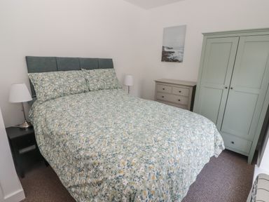 A bedroom with a bed with floral bedding two bedside lamps a chest of drawers and a wardrobe at Gwynfryn in Pen-Clawdd