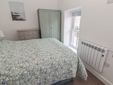 A bedroom with a bed covered with floral bedding a green wardrobe a beige chest of drawers a wall-mounted heater and a window at Gwynfryn in Pen-Clawdd