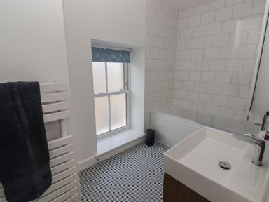 A bathroom with a bathtub sink window with a blue blind and tiled floor at Gwynfryn in Pen-Clawdd
