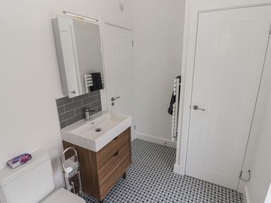 A bathroom with a toilet sink and cabinet a mirror a towel rack and two white doors at Gwynfryn in Pen-Clawdd