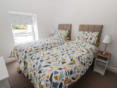 A bedroom with two single beds with patterned bedding and a lamp on a bedside table at Gwynfryn in Pen-Clawdd