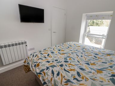 A bedroom with a bed covered in a patterned duvet a wall-mounted TV radiator a closed door and a window with a patterned blind at Gwynfryn in Pen-Clawdd