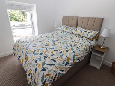A bedroom with a bed with patterned bedding a nightstand and a lamp by a window at Gwynfryn in Pen-Clawdd