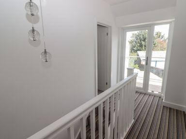 A hallway with striped carpet a white railing a door and glass doors leading outside at Gwynfryn in Pen-Clawdd