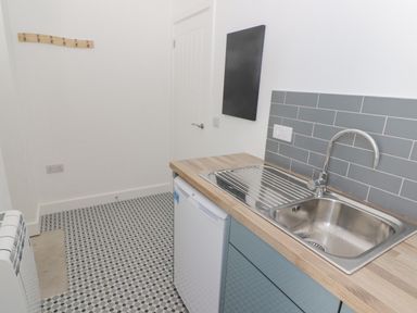 A utility room with a stainless steel sink and faucet a small fridge and a tiled floor at Gwynfryn in Pen-Clawdd