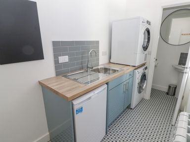 A utility room with a washing machine, dryer, sink, refrigerator, and door leading to a small bathroom at Gwynfryn in Pen-Clawdd