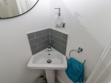 A small corner sink with gray tiles a soap dispenser a turquoise towel on a ring and a round mirror above Gwynfryn Pen-Clawdd