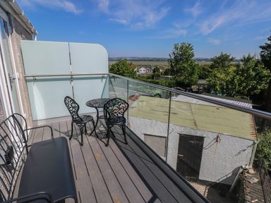 A balcony with black metal table and chairs and a bench overlooking trees and buildings at Gwynfryn in Pen-Clawdd