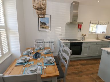 A kitchen with a wooden dining table set for six with blue placemats and grey chairs at Gwynfryn in Pen-Clawdd