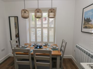 A dining room with a wooden table set for six under three pendant lights and a window with shutters at Gwynfryn in Pen-Clawdd