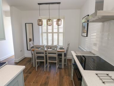 A kitchen and dining area with a table set for six under hanging lights and a window with shutters at Gwynfryn in Pen-Clawdd