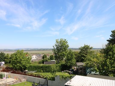 A backyard with trees fences sheds and houses in the distance at Gwynfryn in Pen-Clawdd