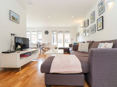 A living room with a brown sectional sofa and cushions a coffee table a tv on a white stand and a dining table with chairs at Garras in Porthtowan