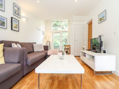 A living room with a gray sofa a white coffee table a white TV stand with a television and a lamp at Garras in Porthtowan