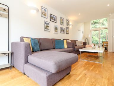 A living room with two brown sofas blue and yellow cushions white coffee table and framed pictures on wall at Garras in Porthtowan