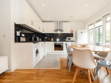 A kitchen with white cabinets a wooden dining table and mixed chairs at Garras in Porthtowan