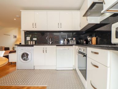 A kitchen with white cabinets black countertop and appliances including washing machine and oven at Garras in Porthtowan