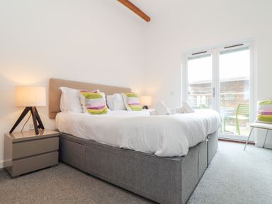 A bedroom with a double bed two bedside tables with lamps and a glass door leading to a balcony at Garras in Porthtowan