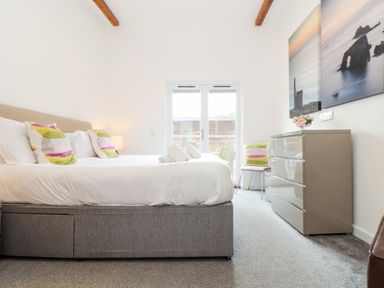 A bedroom with a bed pillows and towels a dresser and a chair by glass doors at Garras in Porthtowan