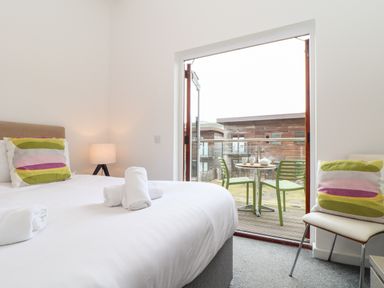 A bedroom with a bed and rolled towels a lamp and an open door leading to a balcony with chairs and a table at Garras in Porthtowan