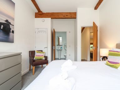 A bedroom with a bed with towels on it a chair with a cushion a dresser and doors leading to a bathroom and another room at Garras in Porthtowan