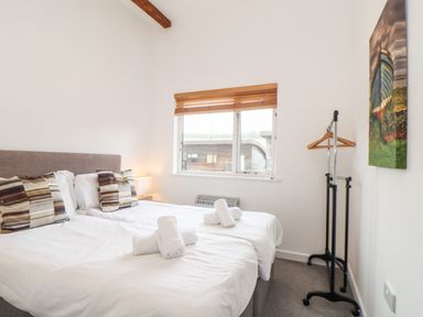 A bedroom with two single beds with rolled towels on them a window with blinds a standing coat rack and a wall painting at Garras in Porthtowan