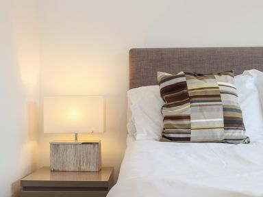 A bedside table with a lamp next to a bed with a striped pillow at Garras Porthtowan
