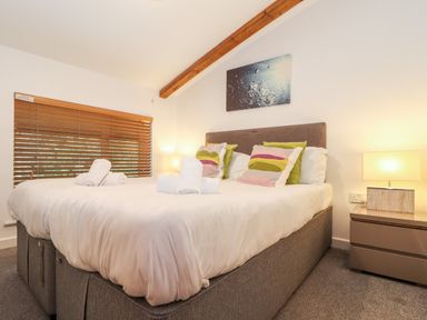A bedroom with a double bed pillows bedside tables with lamps and a painting on the wall at Garras in Porthtowan