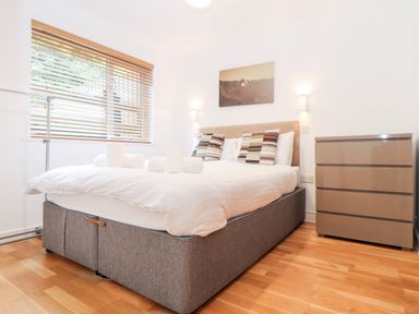 A bedroom with a bed with pillows and rolled towels near a window and a dresser at Garras in Porthtowan