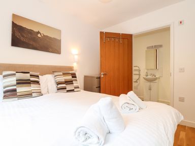 A bedroom with a double bed striped pillows and rolled towels on the bed a partially open wooden door reveals a bathroom with a sink and mirror at Garras in Porthtowan
