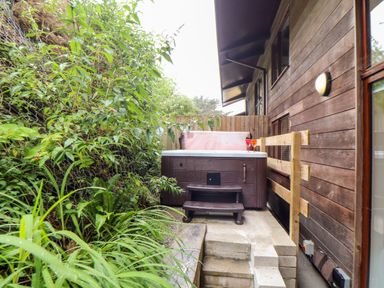 A hot tub on a patio with steps and greenery alongside a wooden house at Garras in Porthtowan