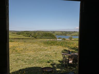 View of a field with wildflowers a wooden table with chairs and a lake in the distance at The Snug in Dulverton