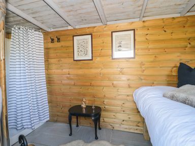 A wooden room with a bed a small black table with decorative items a striped curtain and two framed pictures on the wall at The Snug in Dulverton
