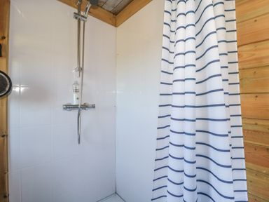 A shower area with a striped curtain a bottle on the shower control and wooden paneling at The Snug in Dulverton