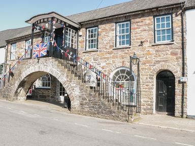An old stone building with an arched stone staircase and a balcony decorated with a Union Jack flag and bunting at The Snug in Dulverton