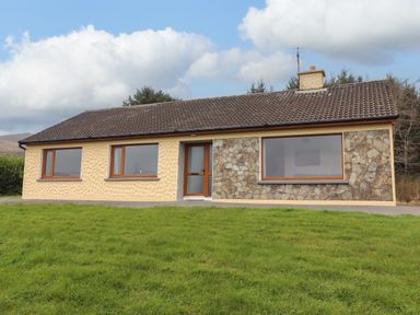 A single-story house with three large windows and a door on a grassy lawn at Gortnamona in Coolnaharragill Lower near Glenbeigh County Kerry