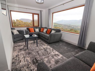 A living room with grey sofas orange and patterned cushions a small table and large windows showing a mountain view at Gortnamona in Coolnaharragill Lower near Glenbeigh County Kerry