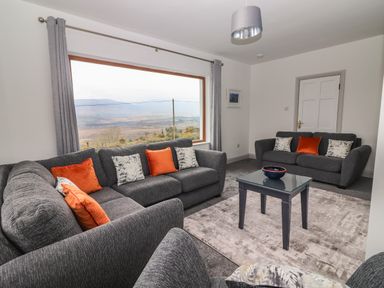 A living room with two grey sofas and orange cushions a glass coffee table and large window showing a landscape view at Gortnamona in Coolnaharragill Lower near Glenbeigh County Kerry