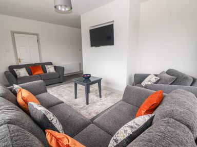 A living room with grey sofas orange and patterned cushions a small table with a bowl a wall mounted television at Gortnamona in Coolnaharragill Lower near Glenbeigh County Kerry
