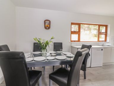 A dining area with a glass table set with plates and glasses black chairs and a kitchen area with a window at Gortnamona Coolnaharragill Lower near Glenbeigh County Kerry