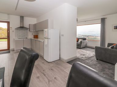 A kitchen with grey cabinets and white refrigerator next to a living room with grey sofas and large window at Gortnamona Coolnaharragill Lower near Glenbeigh County Kerry