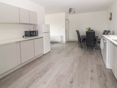 A kitchen and dining area with white cabinets a refrigerator a microwave a washing machine and a dining table with six black chairs at Gortnamona in Coolnaharragill Lower near Glenbeigh County Kerry